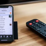 celular exibindo lista de assinaturas ao lado do controle remoto